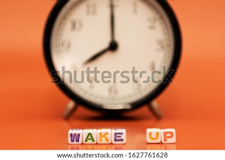 "Wake up" is written by cubes with letters with a black and white classic alarm clock on backside on orange background