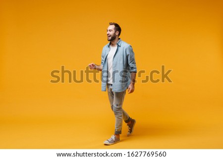 Cheerful laughing young bearded man in casual blue shirt posing isolated on yellow orange wall background studio portrait. People sincere emotions lifestyle concept. Mock up copy space. Looking aside Royalty-Free Stock Photo #1627769560