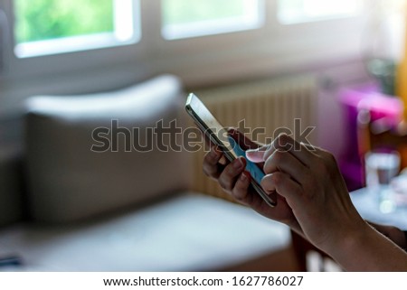 Close-up photo of female using cellphone.Portrait of female hands using mobile,searching or typing message.Shot of young woman using her smartphone near to the window in the living room at home.