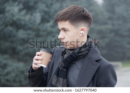 Portrait of a young happy man with cup of coffee on a city promenade, foggy winter weather. Photo in gray tones