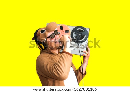 Man in cosplay costume of a cow singing karaoke. Guy in the animal pyjamas sleepwear holding microphone. Funny photo with reel tape recorder. Party ideas. Disco retro music.