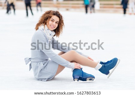 Beautiful curly girl sits on ice in the skates