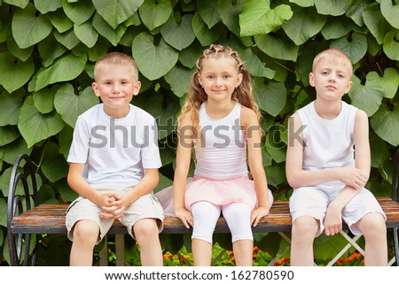 Three children friends sit on bench in summer park