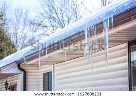 Ice dam in gutter and ice frozen on roof in winter, focus on icicles in foreground  Royalty-Free Stock Photo #1627808221