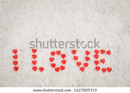 The word Love is made of red glass hearts on white snow. Symbols for Valentine's day, background with snow texture and hearts