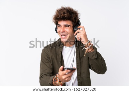 Young handsome man listening music with a mobile over isolated white wall