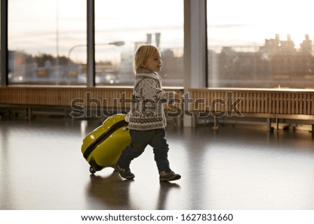 Blonde toddler boy with family, traveling with airplane, running at the airport with suitcase