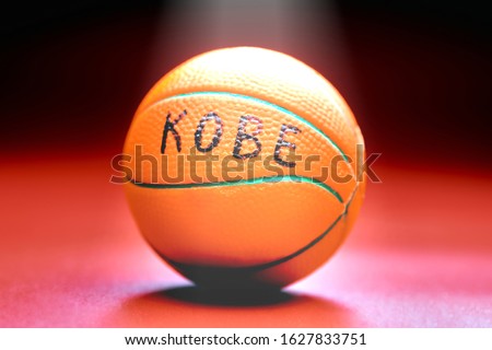 Basketball ball with KOBE inscription, red background. Famous basketball player concept. Ray of light on basketball ball.