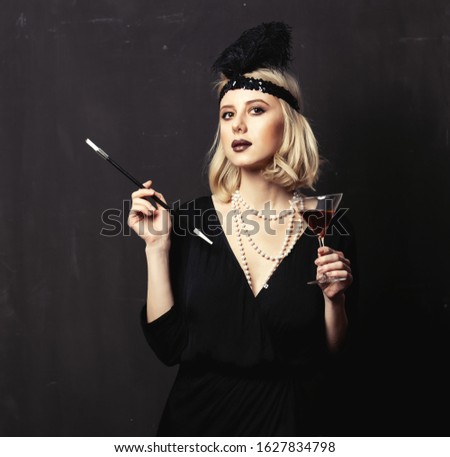 Beautiful blonde woman in twenties years clothes with smoking pipe and cocktail on dark background