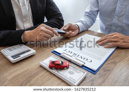 Car rental and Insurance concept, Young salesman giving car's key to customer after sign agreement contract with approved for rent or purchase.