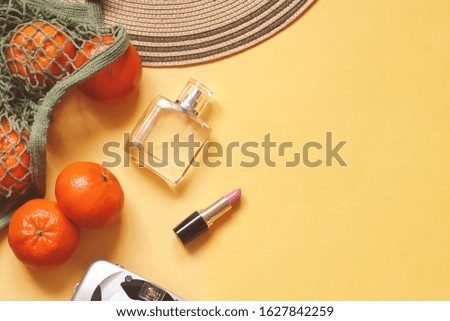 Bag with tangerines, perfume and lipstick on a yellow background. Summer travel photography. Women's items closeup
