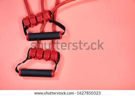 Fitness equipment, rubber expander with black handles on a pink background, space for text