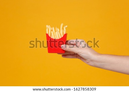 Close up cropped photo of female hold in hand french fries potatoes isolated on yellow orange wall background. Copy space advertising mock up. Proper nutrition or American classic fast food concept