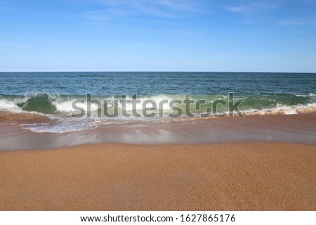 Waves lapping on the beach with clear blue sky & orange sand