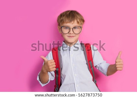 back to school. Happy smiling boy wearing spectacles with a backpack on a pink background.