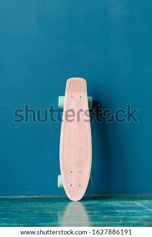 Pink plastic skateboard standing near a blue wall. Plastic female cruiser against blue wall background