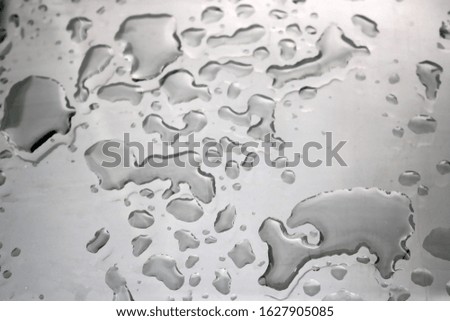 raindrops with irregular shapes on a flat reflective glass surface