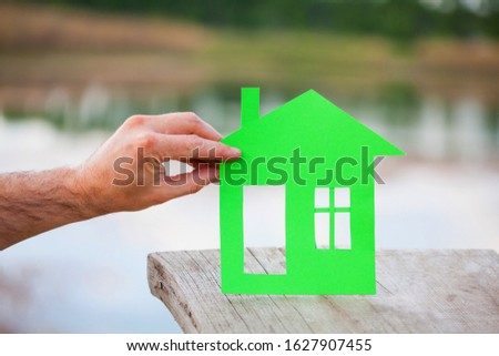 house of paper showing a concept for home and neighborhood. Real estate and family home concept. Ecology house in hands against river, lake, pond background. Eco Friendly House.
