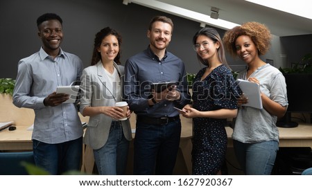Group portrait of smiling multiethnic millennial work team standing together looking at camera in office, happy young multiracial diverse colleagues posing for picture show unity and partnership