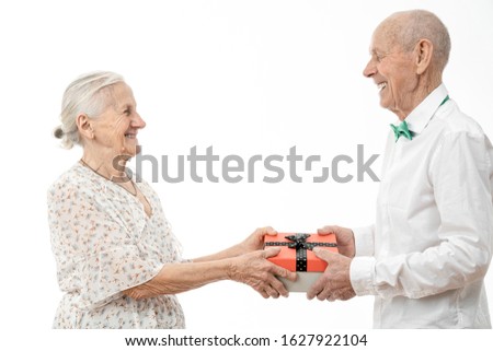 Cheerful elderly couple in white closes looking at each other and exchanging gifts isolated on white background, celebrating valentine's day, studio photo