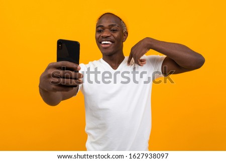 handsome black african man makes selfie on the phone on an orange background with copy space
