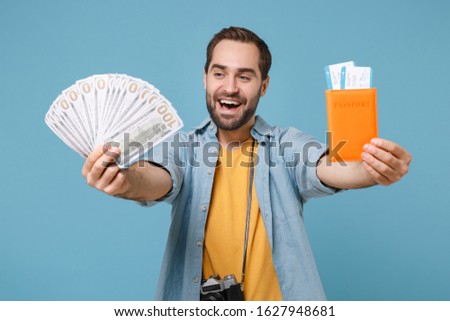 Cheerful traveler tourist man in casual clothes with photo camera isolated on blue background. Passenger traveling on weekends. Air flight journey Hold passport boarding pass ticket fan of cash money