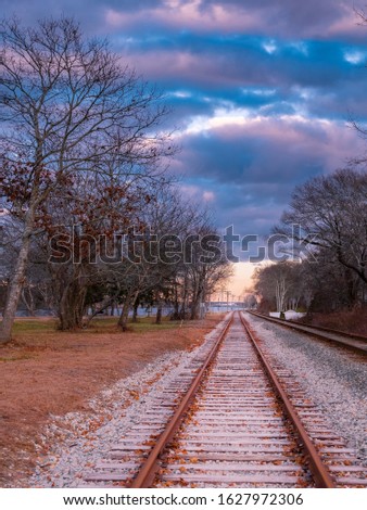 Single railway train track under dramatic cloudy sky in autumn woods 