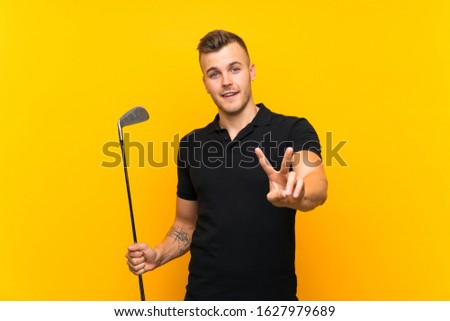 Golfer player man over isolated yellow background smiling and showing victory sign