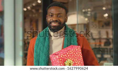 African american young man with Christmas present boxes in cart use phone stand in mall background feel happy smiling shopping internet face close up portrait mobile technology cell slow motion
