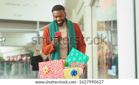 African american young man with Christmas present use phone walk in mall background Christmas tree feel happy smiling shopping internet face close up portrait mobile technology close up slow motion