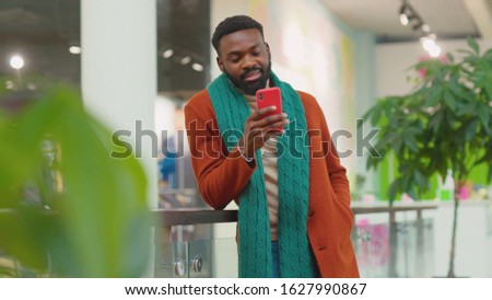 Smiling african american young man use phone walk in mall Christmas time background Christmas tree feel happy shopping internet face close up portrait mobile technology close up slow motion