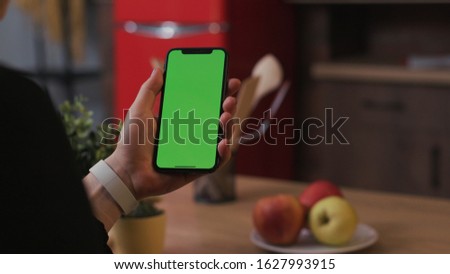 Tokio, Japan - April 7, 2018: Woman hand hold use smartphone with vertical green screen on kitchen at home breakfast browse business food girl house background apple healthy internet slow motion