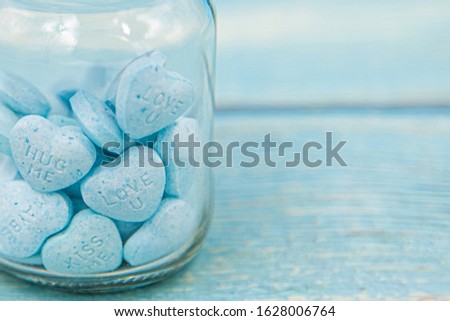 Heart shape message letter candy in glass jar on blue wood background. Valentines day concept.	
