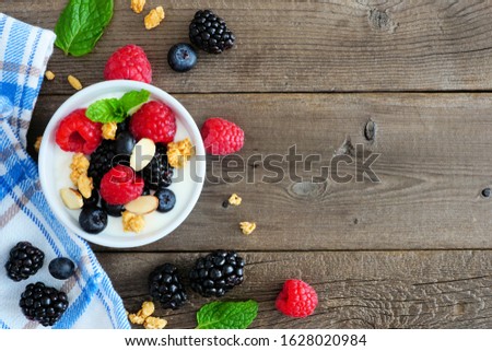 Healthy yogurt with fresh berries and granola. Top view side border against a rustic wood background. Copy space.