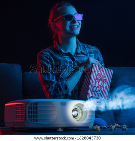 Girl watching a movie. Watching movies in 3D, with glasses. Cinema for home, relaxation and fun. Popcorn. Creative light. Square photo