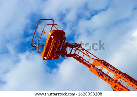 Hydraulic lift platform with bucket of construction vehicle painted in orange color with white clouds and blue sky on background, heavy industry