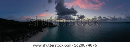 Aerial Beach Sunset with Clouds - Low Altitude Tropical Coastline with Hills / Cliffs - Blue / Purple Sky- Reflective Waters