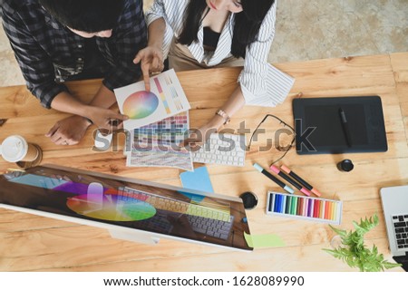 Photo of young creative designer team discussing/brainstorming about color from color palette/color swatches.Top view of creative designer team working desk including designer equipment on it.