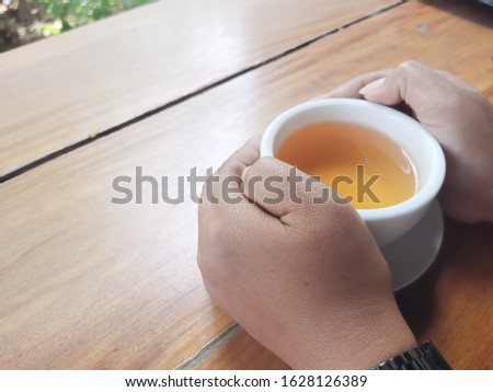A woman's hand that holds a hot tea cup placed on a brown wooden table