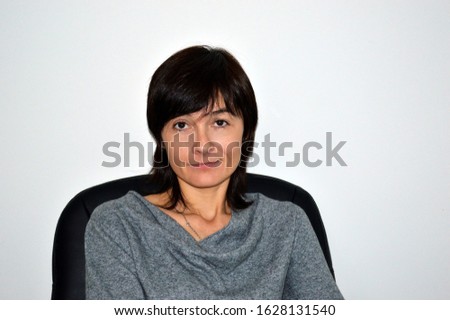 Young beautiful business woman in gray dress sitting on the black leather armchair and confidently looking into the camera on white background