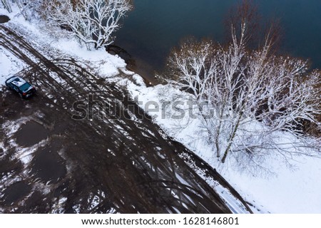 aerial view of lake with dark water and bare trees on coastline, covered with snow