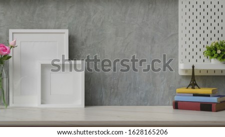 Close up view of stylish workplace with copy space, mock up frames and decorations on marble desk with shelf on grey loft wall background 