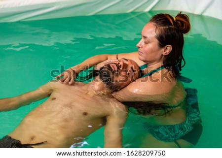 Young man in swimming costume floating on water with eyes closed while receiving aqua treatment massage from young therapist in swimming pool Royalty-Free Stock Photo #1628209750