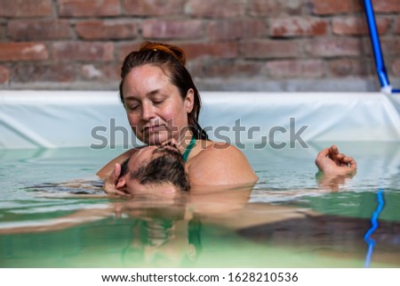 Close-up of female therapist doing facial water massage of young bearded man in swimming pool relaxing with eyes closed during aqua therapy session Royalty-Free Stock Photo #1628210536