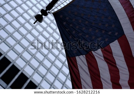 A low angle shot of the united states flag on the pole with a blurred building in the background