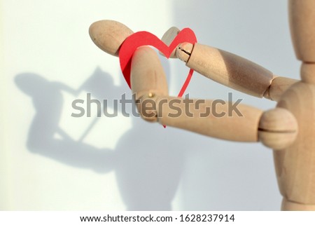 Red paper heart on the hands of a wooden mannequin. Trendy minimal concept of Valentine's day, love, real feeling. Copy space. Shadows in the background.