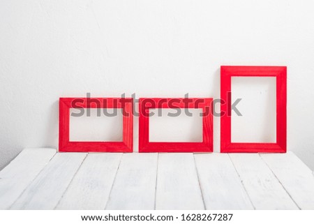 three empty red picture frames on white wooden table