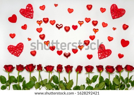 Heart symbol made of various red hearts and sweets with fresh red rose flowers on white background. Greeting card, mock up. Love, romance or Valentine's day concept. Flat lay, top view, copy space
