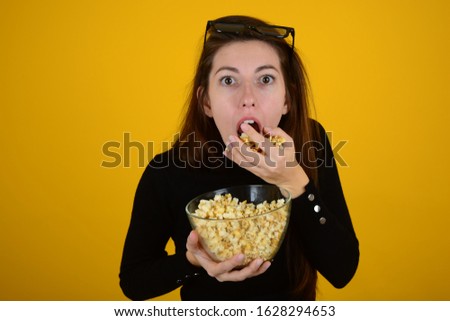 surprised woman eating popcorn watching a film on a yellow background portrait