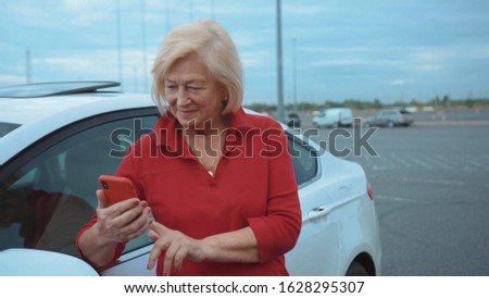 Portrait senior woman stand near car use red cell phone smile businesswoman blonde people smartphone cellphone communication internet search lady mobile browse network online slow motion
